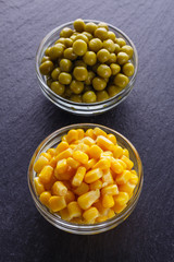 canned corn and green peas in a glass bowl on a dark stone background