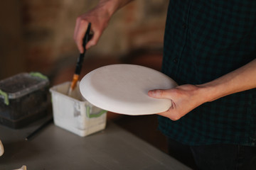 Potter making ornament on ceramic plate. Professional male potter draw a pencil on ceramic product