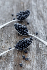 Black currants in vintage metal spoons on wooden background