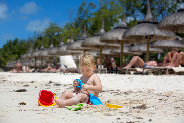 Cute toddler baby boy playing with beach toys on tropical beach