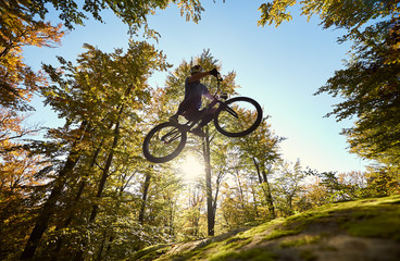 Low angle view of professional sportsman cyclist jumping on trial bicycle, male rider making...