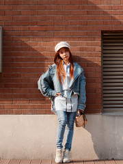 Street photography of a cute Chinese young woman in jeans and white hat with brick wall background, female portrait.