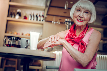 Delighted joyful elderly woman using hand cream