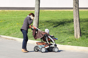 Young mother with a child in a pram talking on a mobile phone. Walk a girl with a son or daughter. Dependence on social networks and modern technologies. Mobile communication between people.