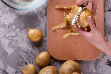 A young woman in an apron peeling potatoes