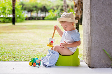 Sweet toddler boy, sitting on potty on a back porch in a holiday resort patio