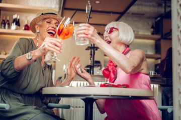 Low angle of positive happy women cheering with drinks