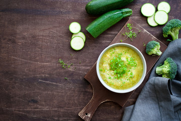 Bowl of broccoli cream soup or zucchini. Brown cutting board and dark plywood background