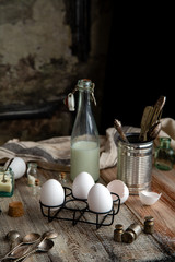 Still life with vintage bottle of milk, black metal stand with eggs, jar with kitchen utensils 