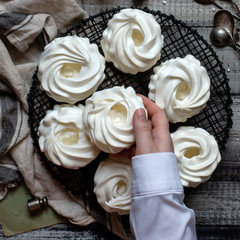 Overhead shot of homemade white mini meringue desserts pavlova on wicker metal stand on grey wooden table