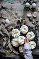 Overhead shot of homemade white mini meringue desserts pavlova on wicker metal stand on grey wooden table