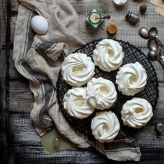 Overhead shot of homemade white mini meringue desserts pavlova on wicker metal stand on grey wooden...