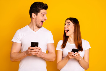 Portrait of his he her she two nice attractive lovely stylish trendy cheerful cheery positive people using new cool gadget device wow isolated over vivid shine bright yellow background