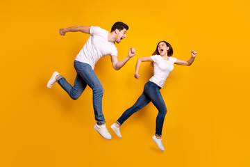 Full length side profile body size photo funky she her he him his pair jumping high hurry shopping raised fists yell scream shout loud wear casual jeans denim white t-shirts isolated yellow background