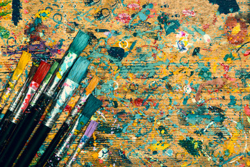 Obraz premium Top view. Old stained artist table and paintbrushes with copy space. Artistic background