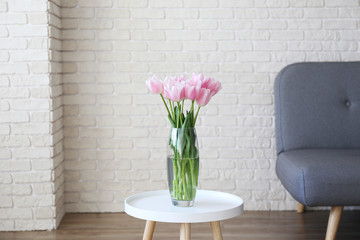 Empty apartment with minimal loft style interior, wooden floor and glass vase with bouquet of tulips on foreground and blank wall with a lot of copy space for text on background. Close up.
