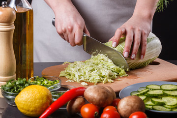 A young woman in a gray apron cuts chinese cabbage