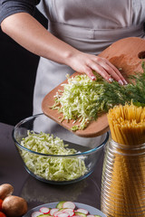 A young woman in a gray apron cuts chinese cabbage