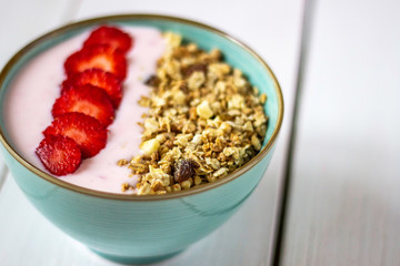 Granola with strawberries on a white wooden backdrop.