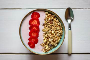 Granola with strawberries on a white wooden backdrop.