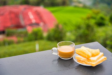 Coffee and deep-fried dough stick on wood table at the tea plantation in morning time.Thailand.