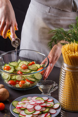 A young woman in a gray apron adds an oil to a Chinese cabbage salad