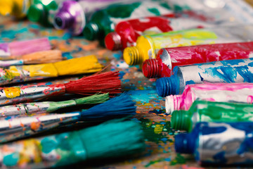 Fototapeta premium Stained paintbrushes and acrylic pain tubes on artist table. Artistic background
