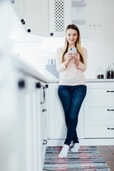 Fototapeta na wymiar Young beautiful woman using cell phone in the kitchen