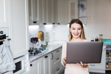 Smiling young woman using laptop in the kitchen at home