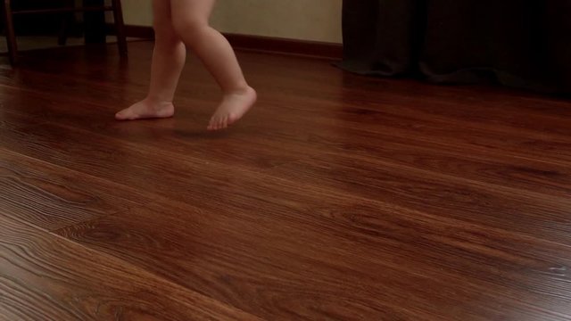 Legs barefoot of the child revolve around its axis in slow motion close-up without any help . Baby began to take his first steps close-up on his feet