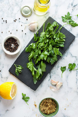 Green fresh parsley on black slate with ingredients and pepper. View from above.