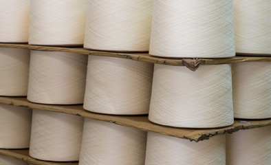 Textile threads industry, Rolls of industrial cotton fabric for clothing cloth textile manufacture on machine in a factory, large group of bobbin thread cones of cotton yarn in the warehouse