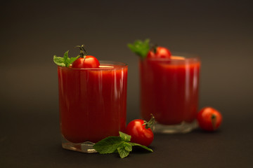 Two glasses of tomato juice with cherry tomatoes and mint with a black background