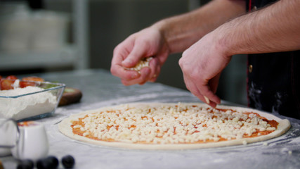 Restaurant kitchen. A chef putting cheese on the pizza