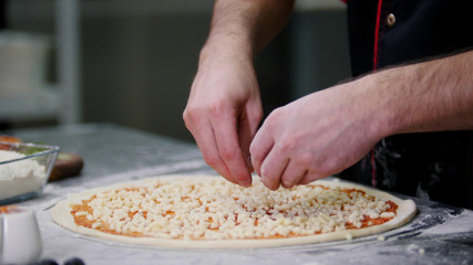 A chef putting cheese on the pizza. Aligning the cheese layer on the pizza