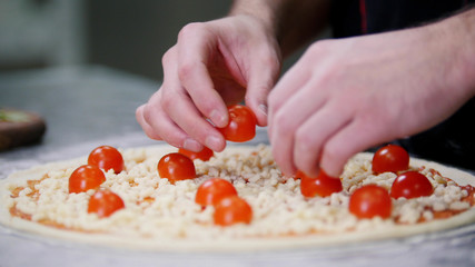 Restaurant kitchen. A chef putting cherry tomatoes on the pizza