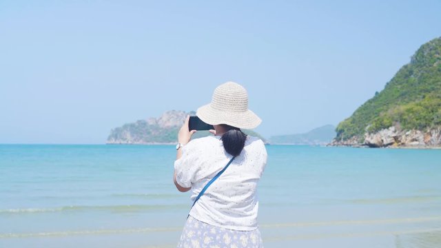 Asian lady try to take a picture at the beautiful sea and beach. shot at the back. Island at background.