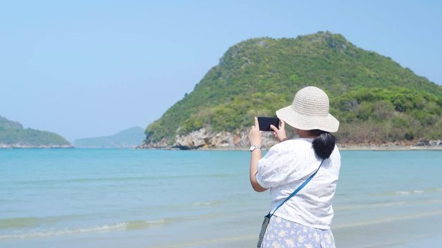 Asian lady try to take a picture at the beautiful sea and beach. Island at background.