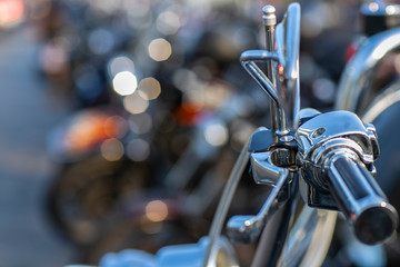 The chromed handlebar of a motorcycle.  View of motorcycle handlebar in the background many motorbikes blurred. 