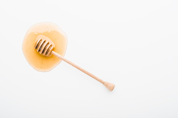 Wooden honey dipper on a honey stain on white background