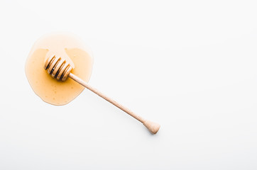 Wooden honey dipper on a honey stain on white background