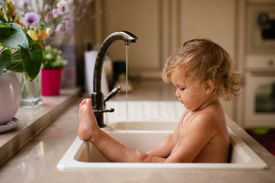 Baby Taking Bath In Kitchen Sink. Child Playing With Foam And Soap Bubbles In Sunny Bathroom With Window. Little Boy Bathing. Water Fun For Kids. Hygiene And Skin Care For Children