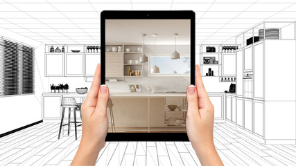 Hands holding tablet showing modern white and wooden kitchen. Blueprint CAD sketch background,...