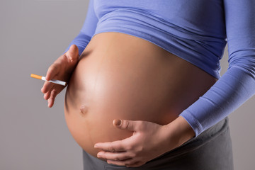 Image of pregnant woman smoking cigarette on gray background.