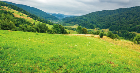 Fototapeta na wymiar countryside in mountain on a cloudy summer day. settlement in the distant valley. beautiful landscape with rural hay fields on hills near the forest
