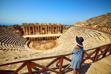 Back view of woman traveler in hat looking at amazing Amphitheater ruins in ancient Hierapolis,...
