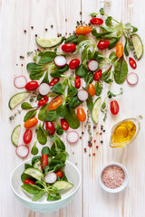 Fresh raw tomatoes, cucumbers, baby spinach and seasonal greens. Top view, close-up on white wooden background.
