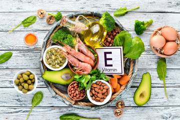 Food containing natural vitamin E: Spinach, parsley, shrimp, pumpkin seeds, eggs, avocados, broccoli. Top view. On a white wooden background. - obrazy, fototapety, plakaty