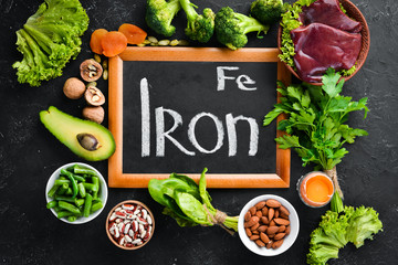 Food containing natural iron. Fe: Liver, avocado, broccoli, spinach, parsley, beans, nuts, on a black stone background. Top view.