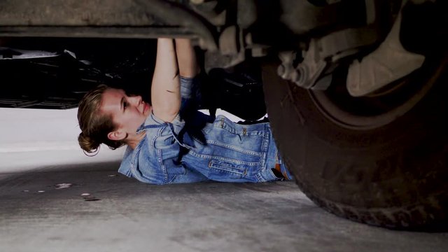 A woman on the ground underneath a vehicle, having fun while going through routine maintenance, 23.98 fps.